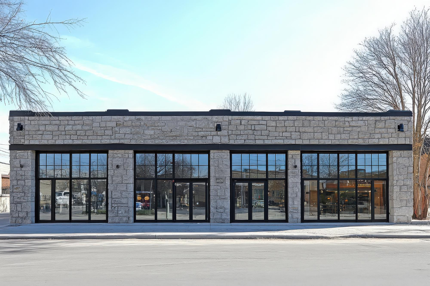 Modern commercial building with gray stone exterior walls, large black-framed glass windows, and flat roof design