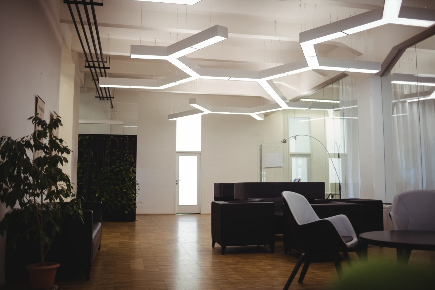 Modern commercial interior with geometric LED ceiling lights, black furniture, hardwood floors, and glass partitions
