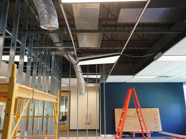 Commercial construction site with exposed ceiling, blue accent wall, orange ladder, and scaffolding during tenant improvement work