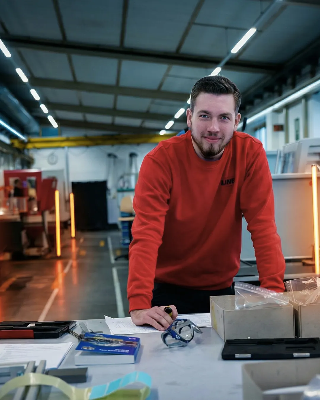 Ein Auszubildender von LINCK ist an eine Werkbank gelehnt, während er in die Kamera lächelt. 