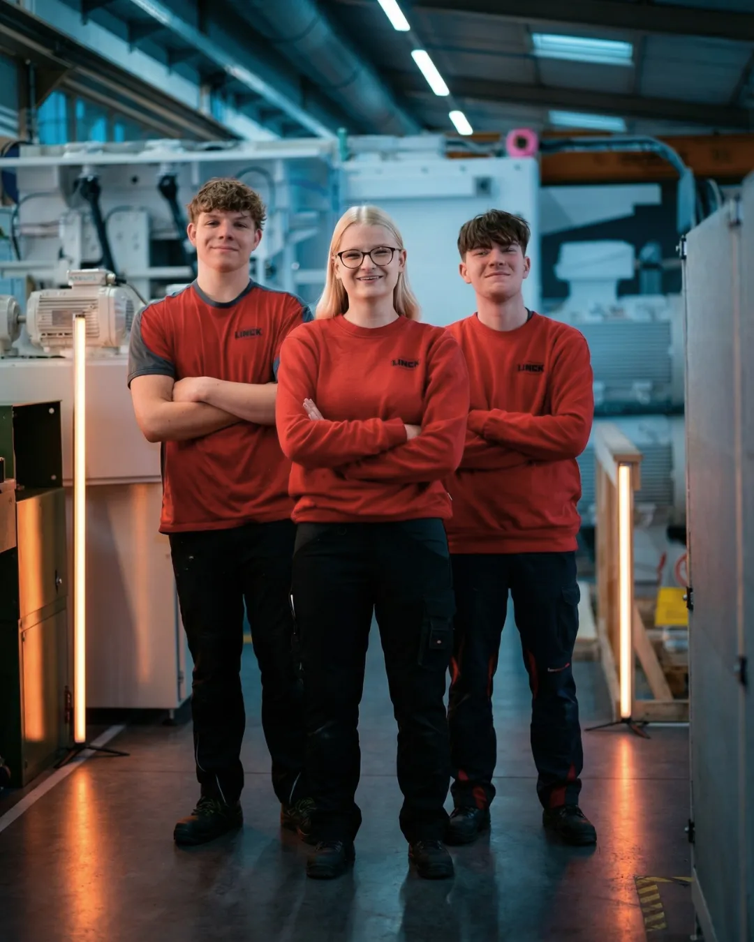 Drei Auszubildende von LINCK stehen vor einer Maschine und lächeln in die Kamera.