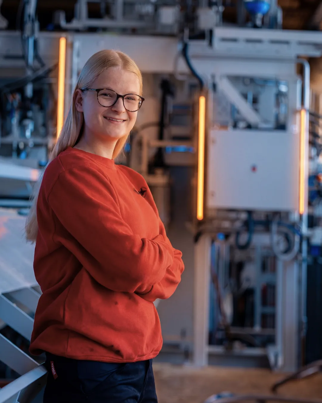 Eine Auszubildende von LINCK lehnt an einer Maschine und lächelt in die Kamera.