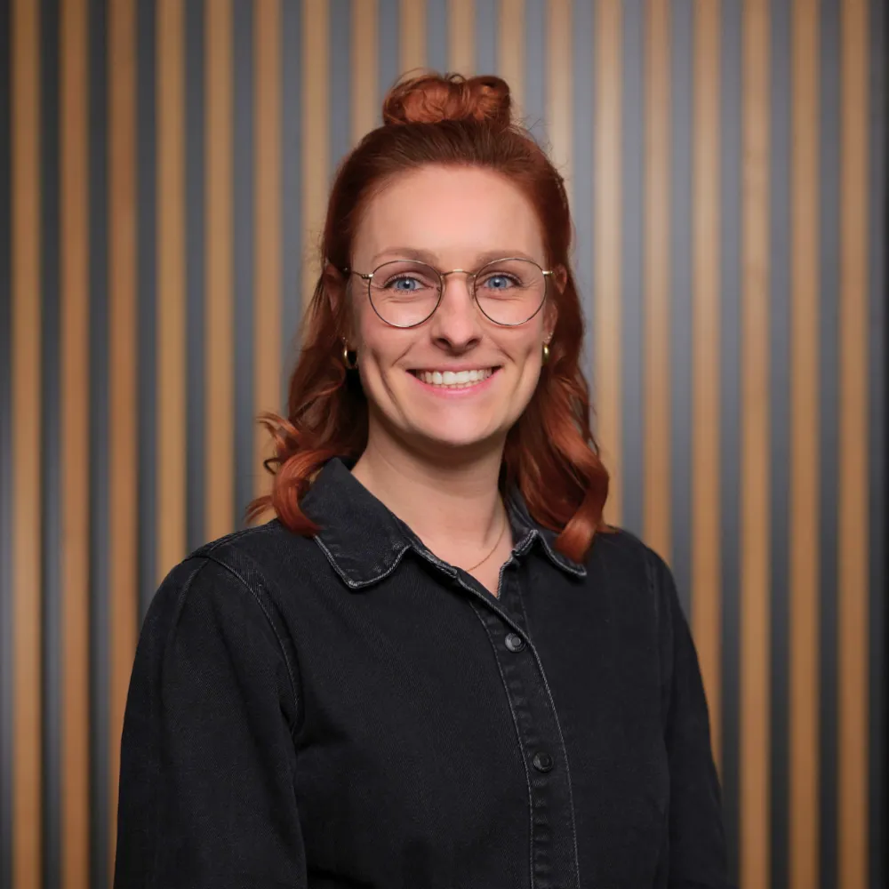 Personalmitarbeiterin Selina Haller lächelt in die Kamera, vor einem Hintergrund mit hölzernem Akustikpanel.