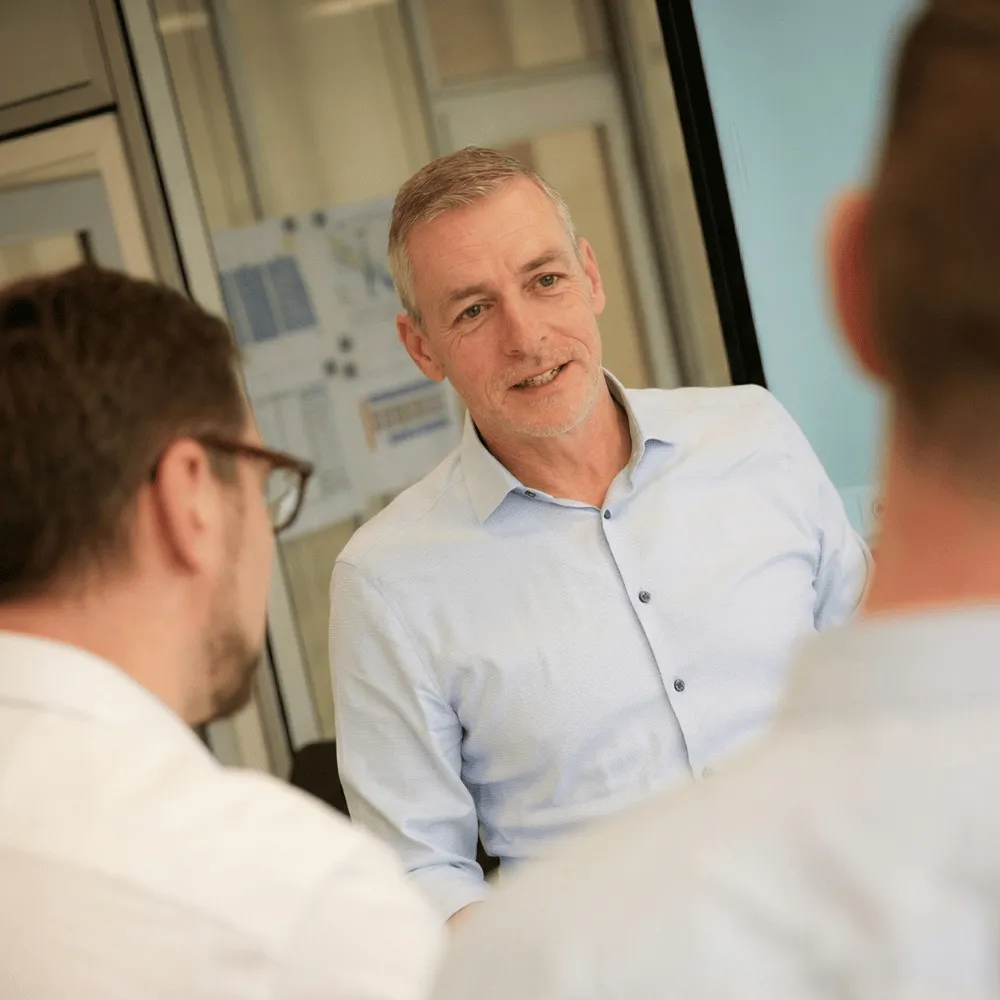 LINCK-Mitarbeiter im hellblauen Hemd im Gespräch mit zwei Kollegen vor einem aufgehängten Projektplan