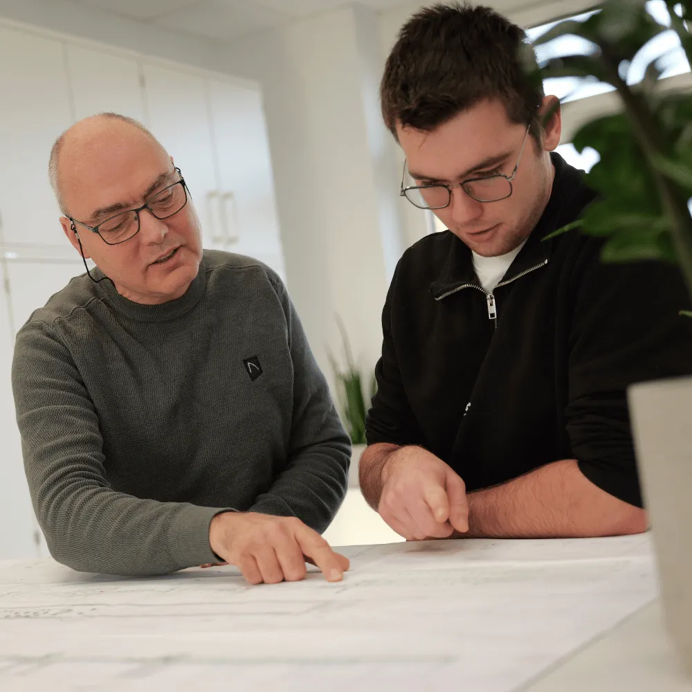 Zwei Kollegen bei LINCK analysieren gemeinsam einen Projektplan, während ein Mitarbeiter mit Brille auf einen Bereich des Plans zeigt