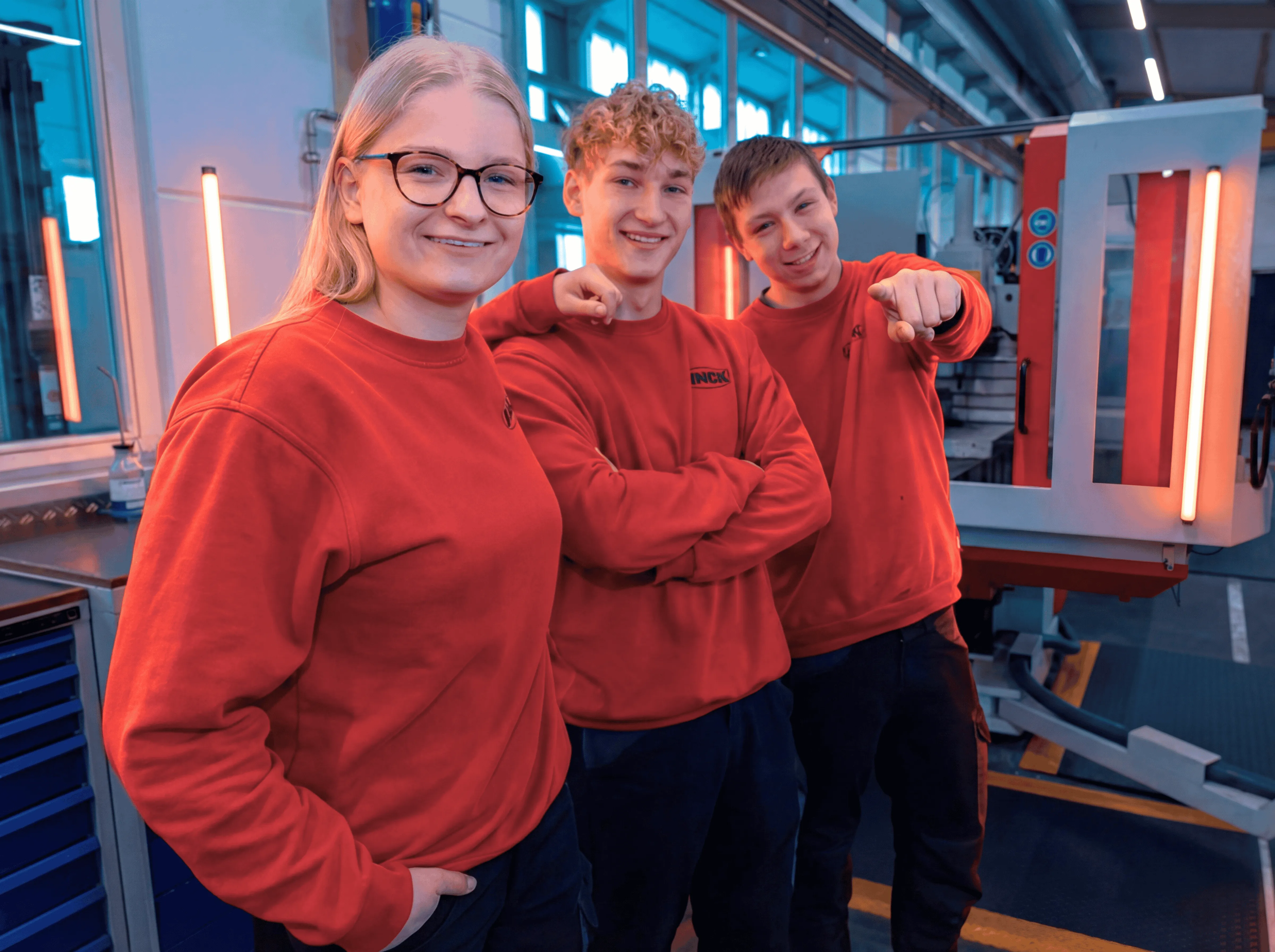 Drei Auszubildende bei LINCK stehen beieinander in roten Pullis, lehnen aneinander und schauen lächelnd in die Kamera