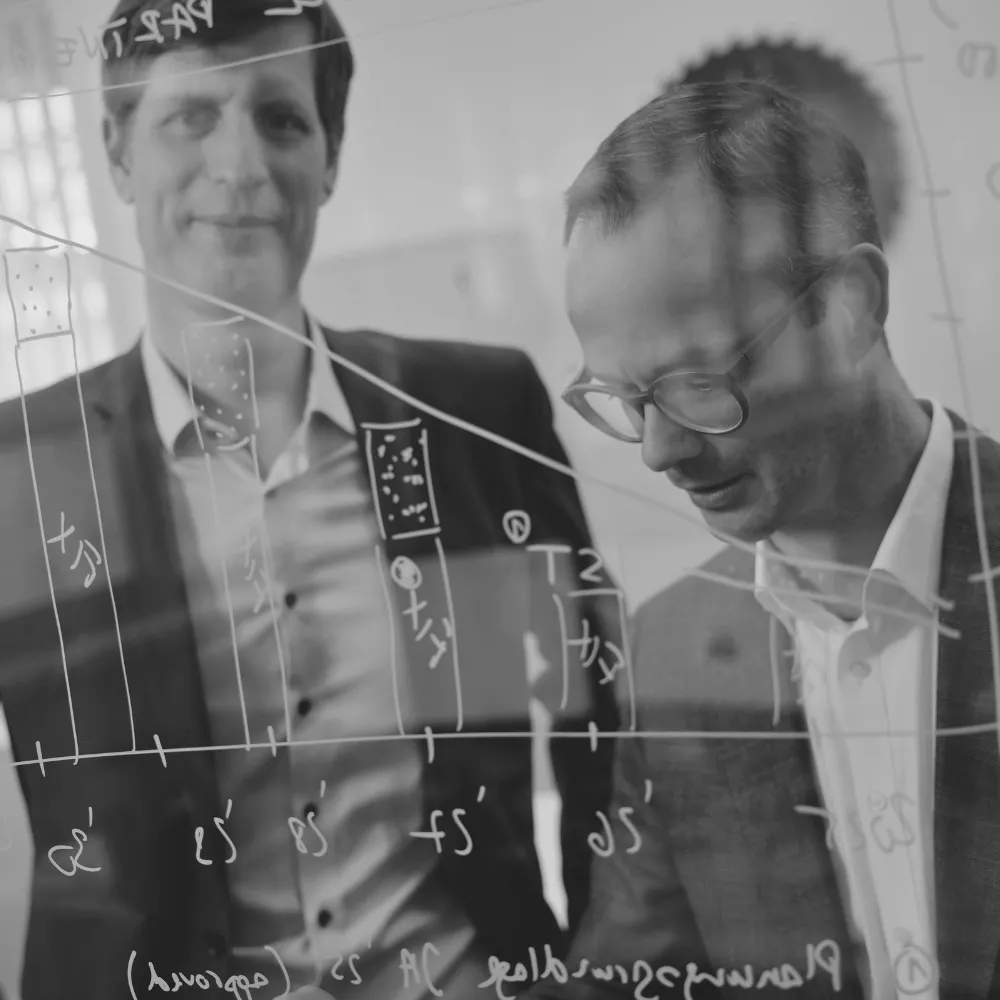 Zwei CEOs von LINCK stehen im Anzug hinter einer Glaswand, markieren eine Grafik und besprechen gemeinsam den Verlauf der Kurve