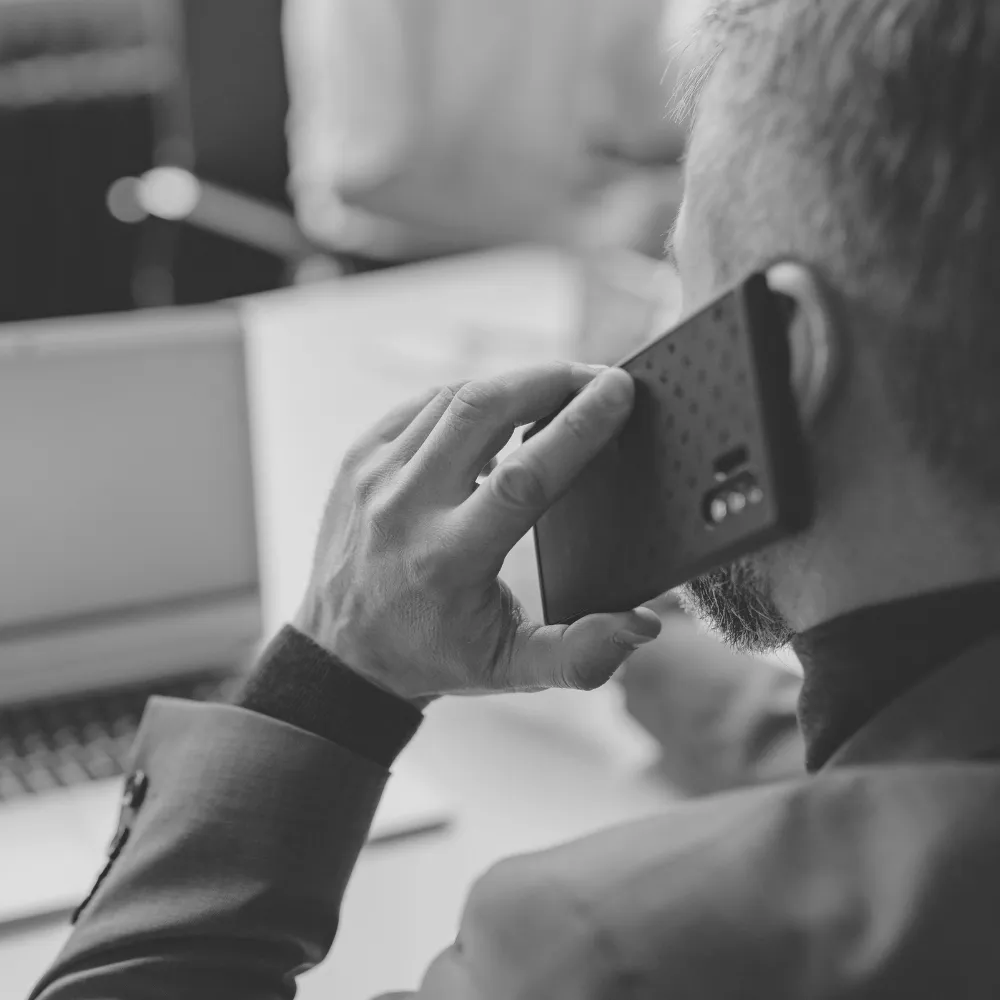 Mann telefoniert mit dem Smartphone vor geöffnetem Laptop im beruflichen Arbeitsumfeld