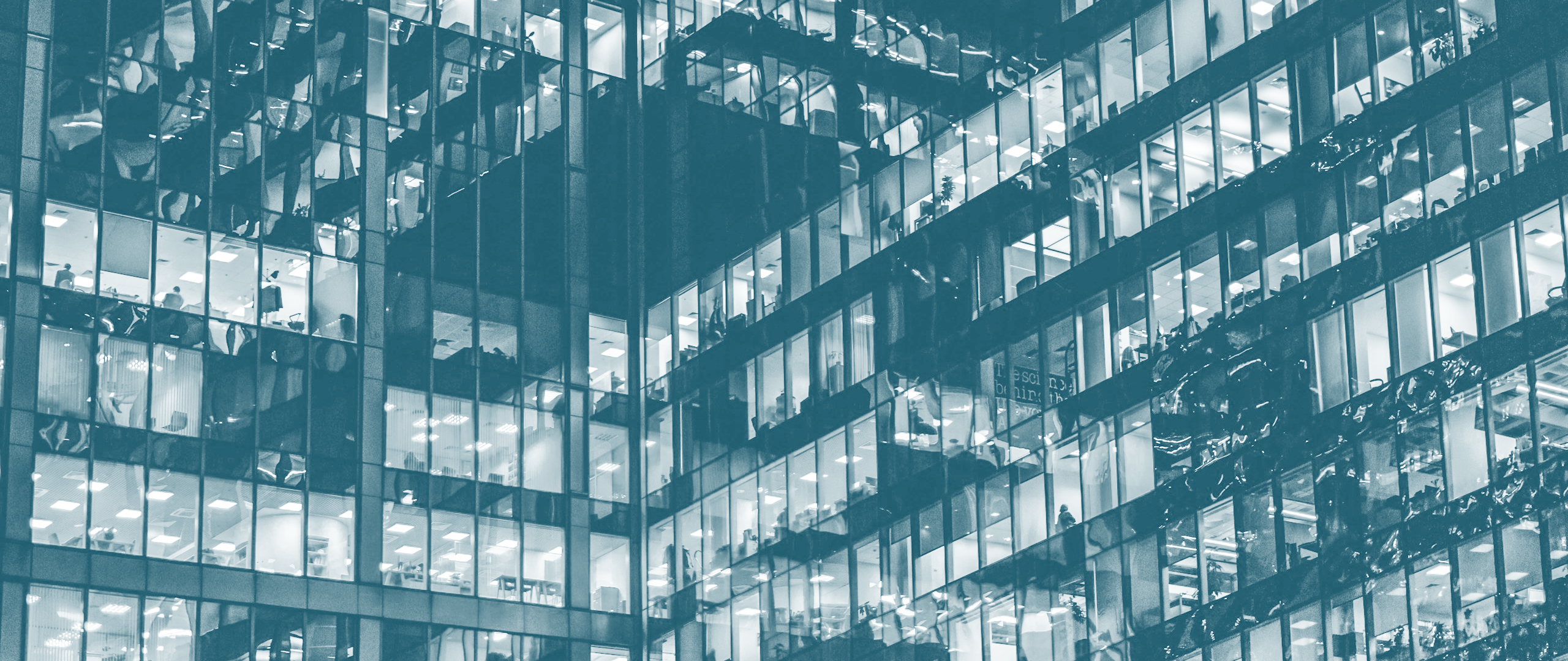 Exterior view of a modern office building with many illuminated windows showing office interiors at night.