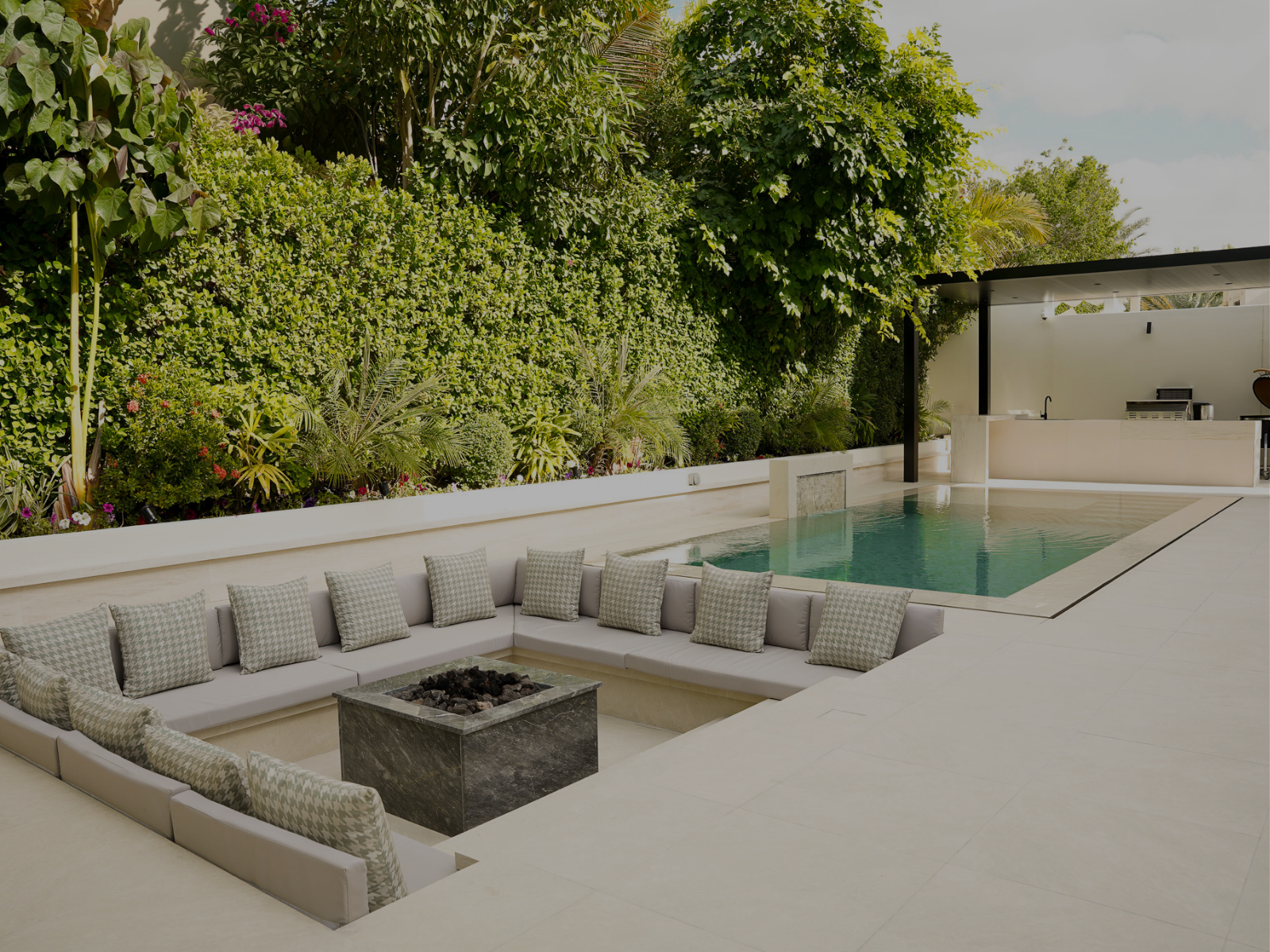 Modern pool water feature with a rectangular stone frame cascading water into a pool, surrounded by lush greenery.