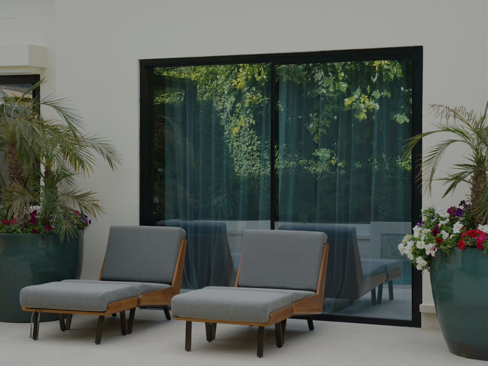 Modern outdoor kitchen with white countertop and black canopy next to a small pool and lush green plants.