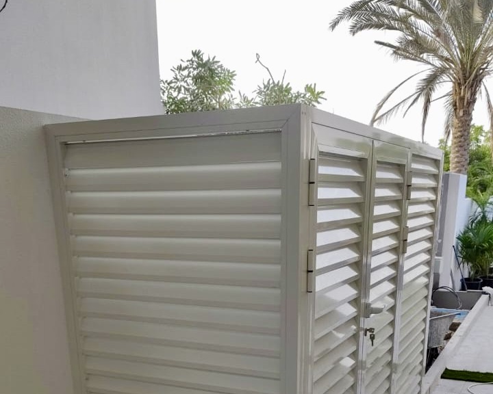White louvered outdoor storage cabinet with two people working nearby in a backyard setting.