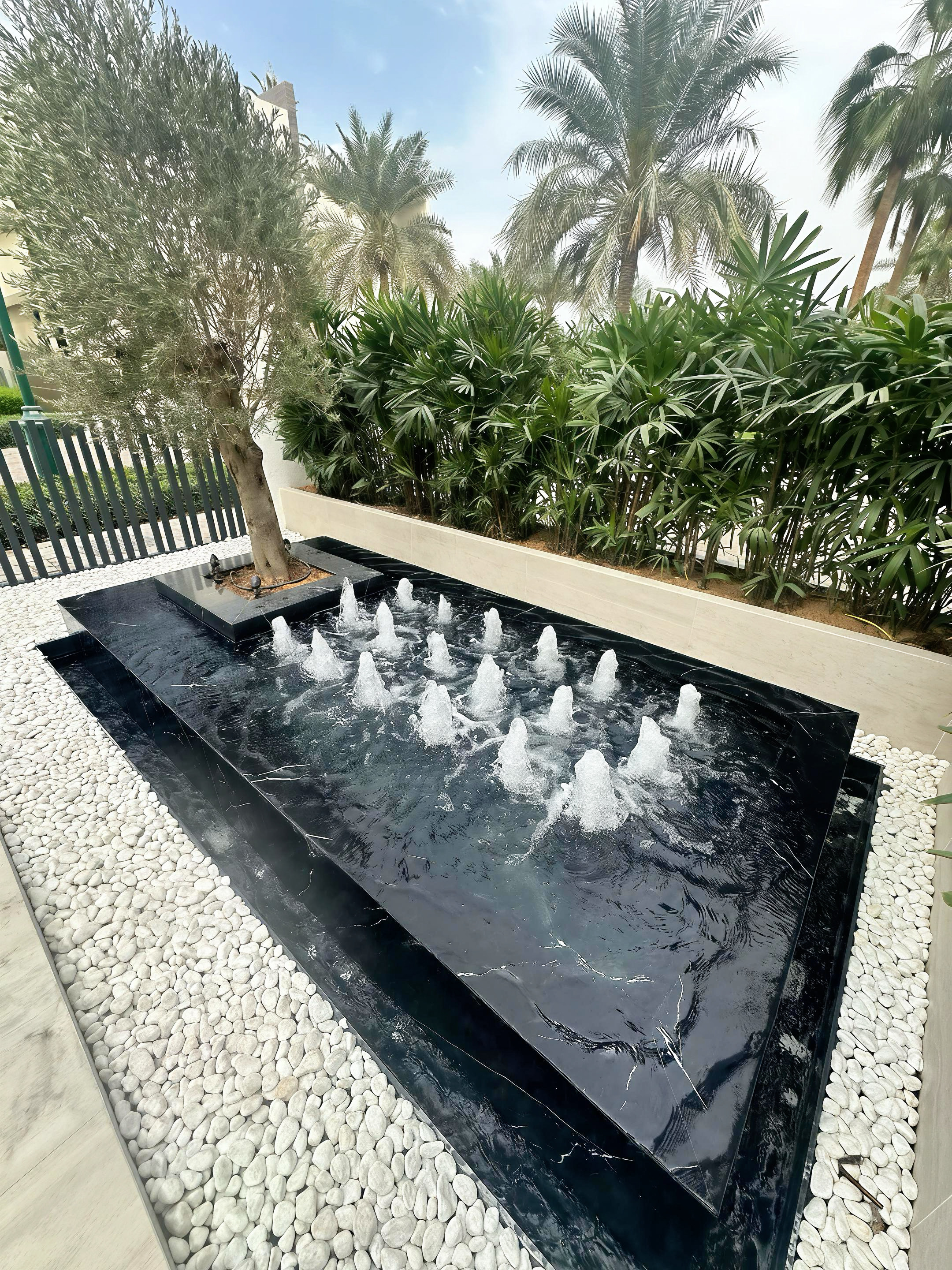 Modern outdoor pool area with white cushioned seats on a wooden platform and a swing sofa surrounded by greenery.
