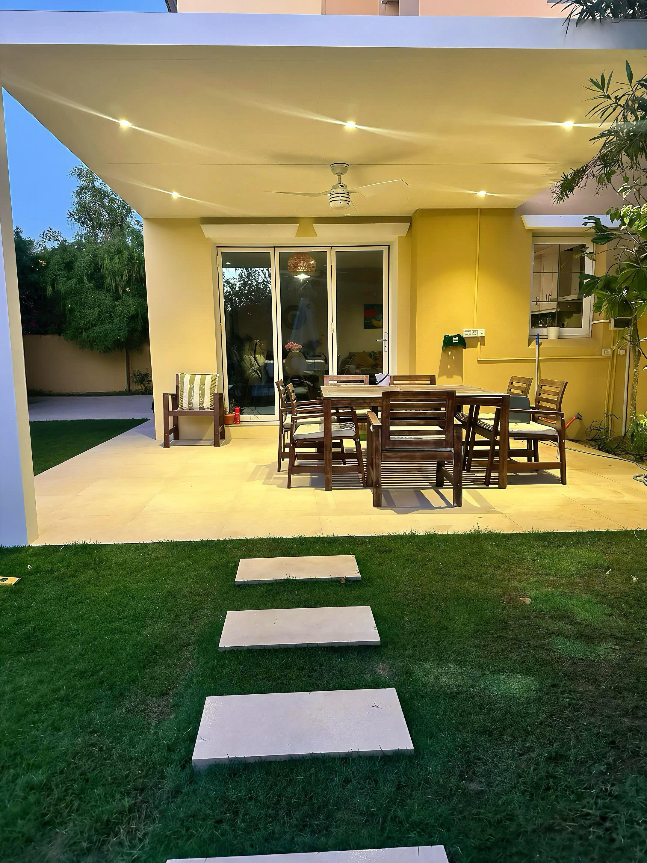 Construction site in a garden with a large excavated pit surrounded by dirt piles and green bushes against a yellow wall.