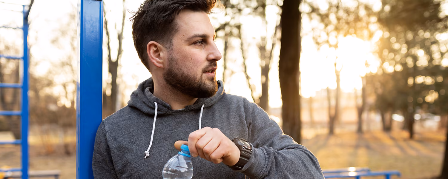 Un homme se reposant après une séance de sport en plein air, bouteille d'eau à la main