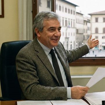 Uomo, responsabile comunale, in giacca grigia e cravatta seduto a una scrivania che tiene un foglio in mano.