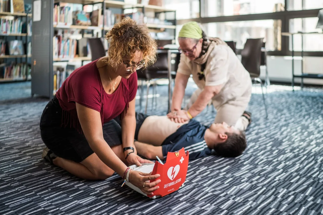 Due donne eseguono la rianimazione cardiopolmonare su un uomo sdraiato mentre una controlla il defibrillatore Schiller FRED PA-1.