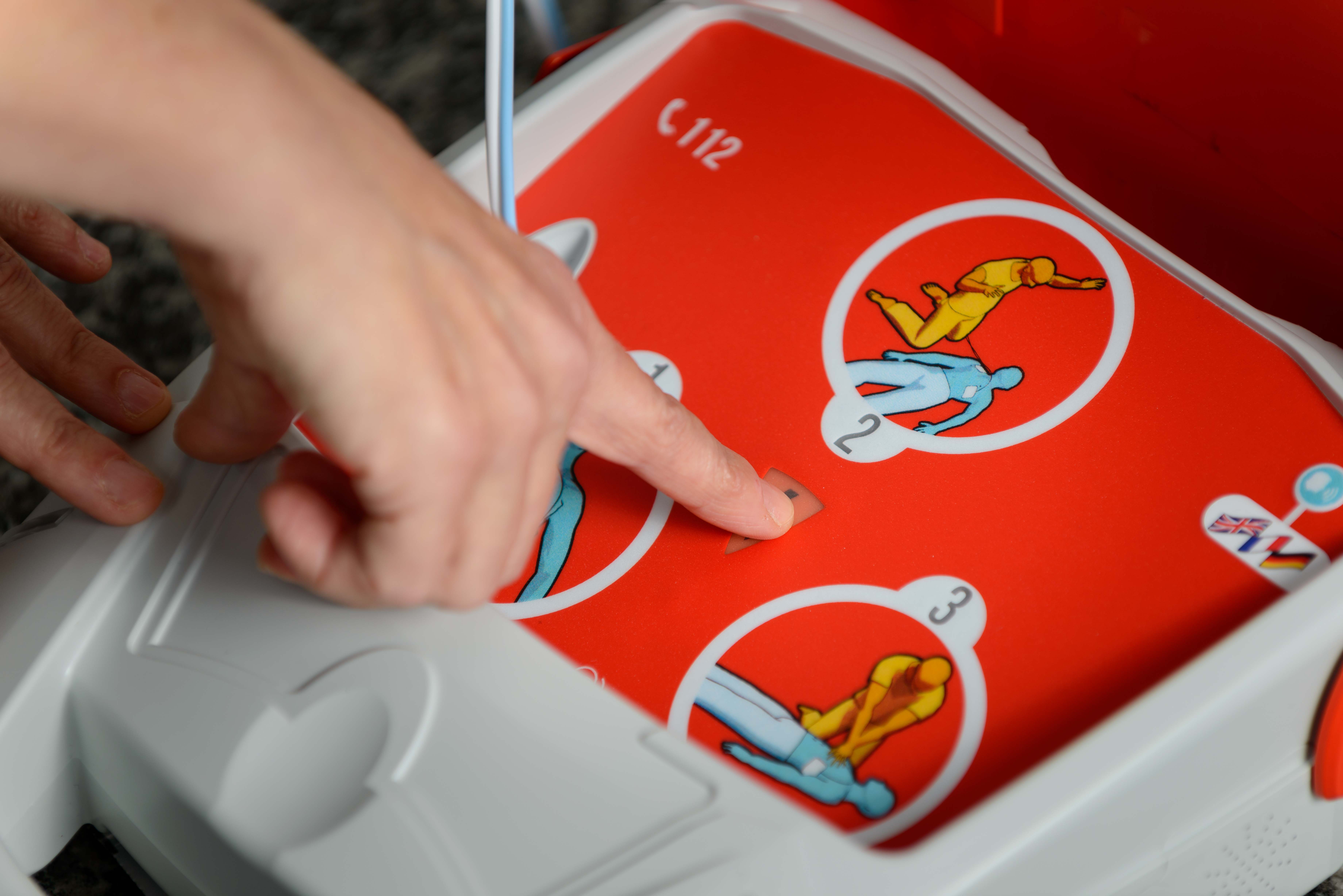 Defibrillatore DAE Schiller FRED PA-1. Aperto con dito che preme tasto shock.