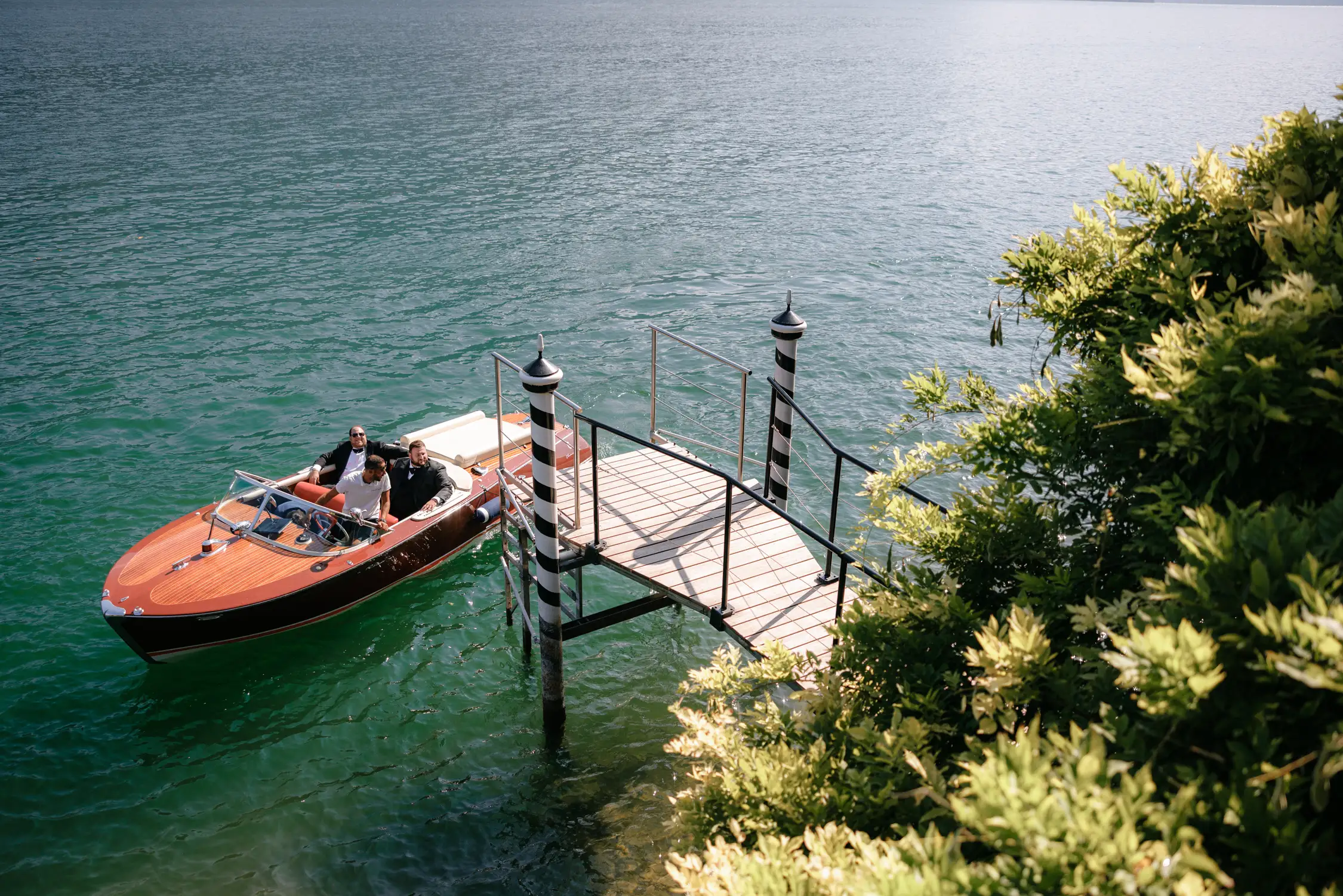 Classic wooden boat docked at striped pier surrounded by green water and plants