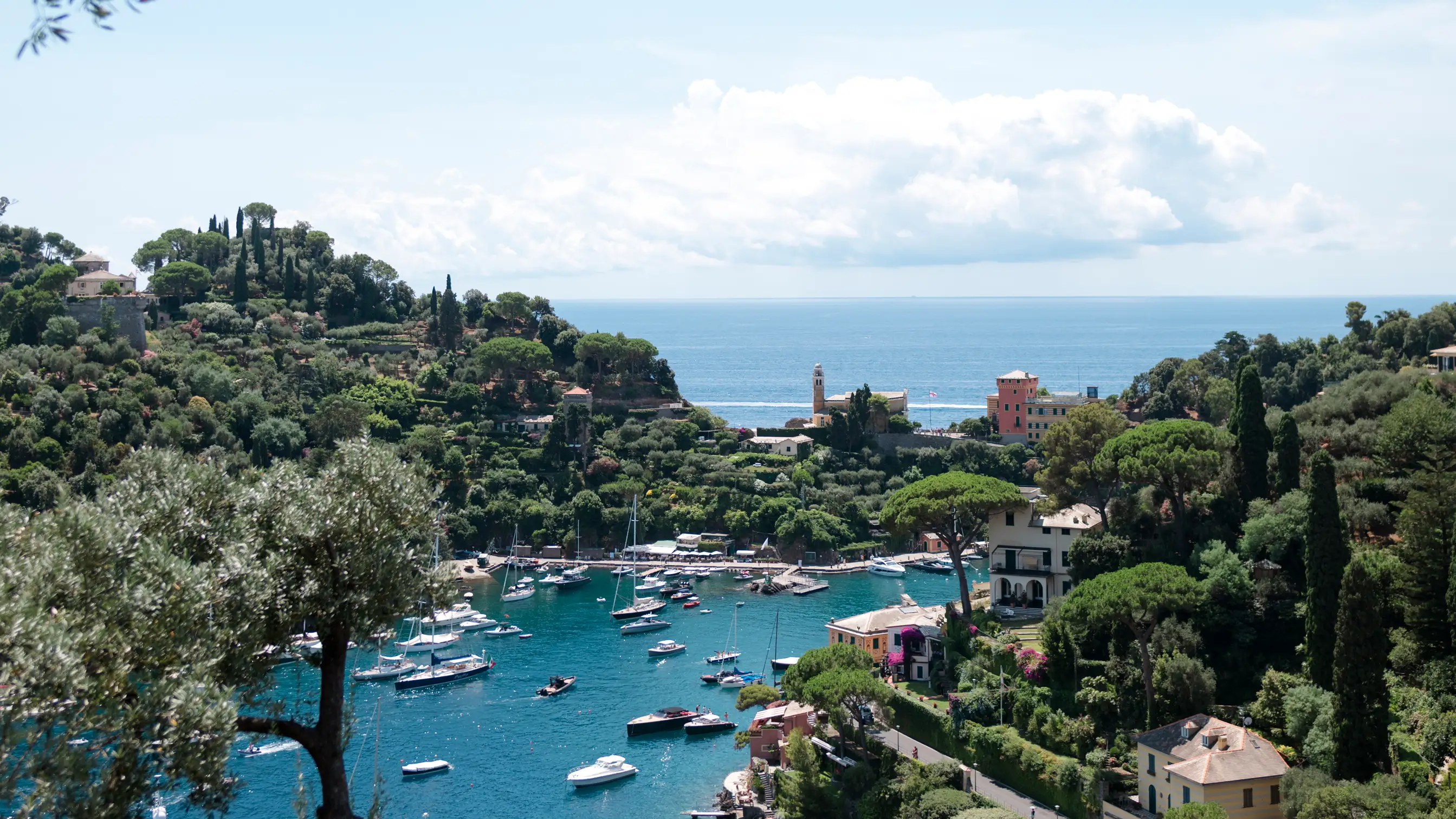 Scenic Italian coastal town with turquoise bay and boats, lush green landscape in Portofino
