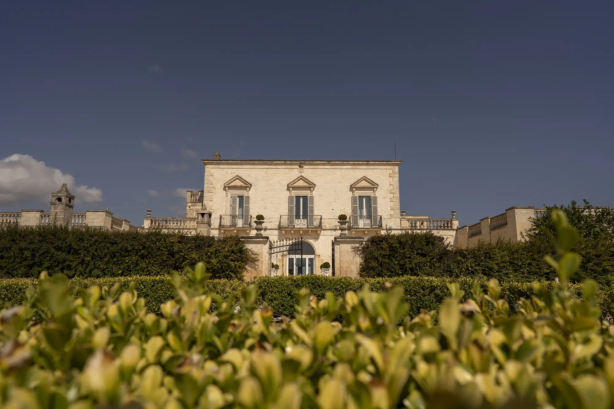Elegant Italian villa with manicured gardens and hedges under blue sky in Apulia
