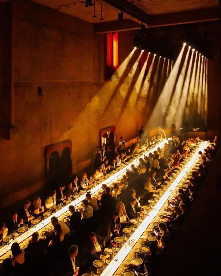 Long communal dinner table illuminated by dramatic golden light beams