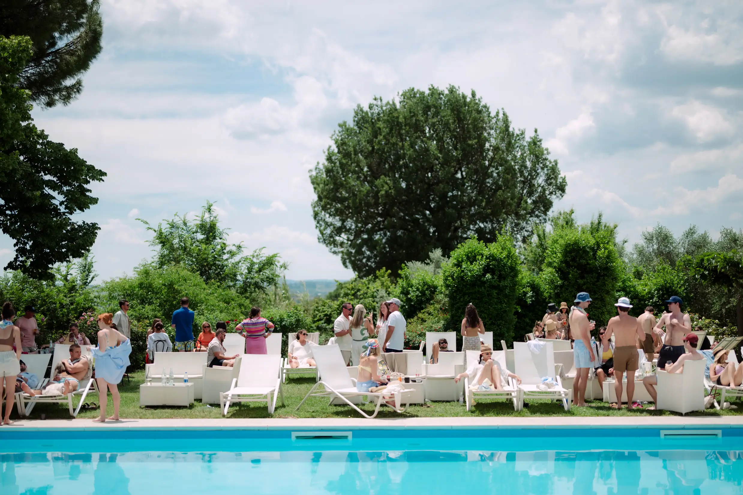 Sunny poolside gathering with people relaxing on white lounge chairs