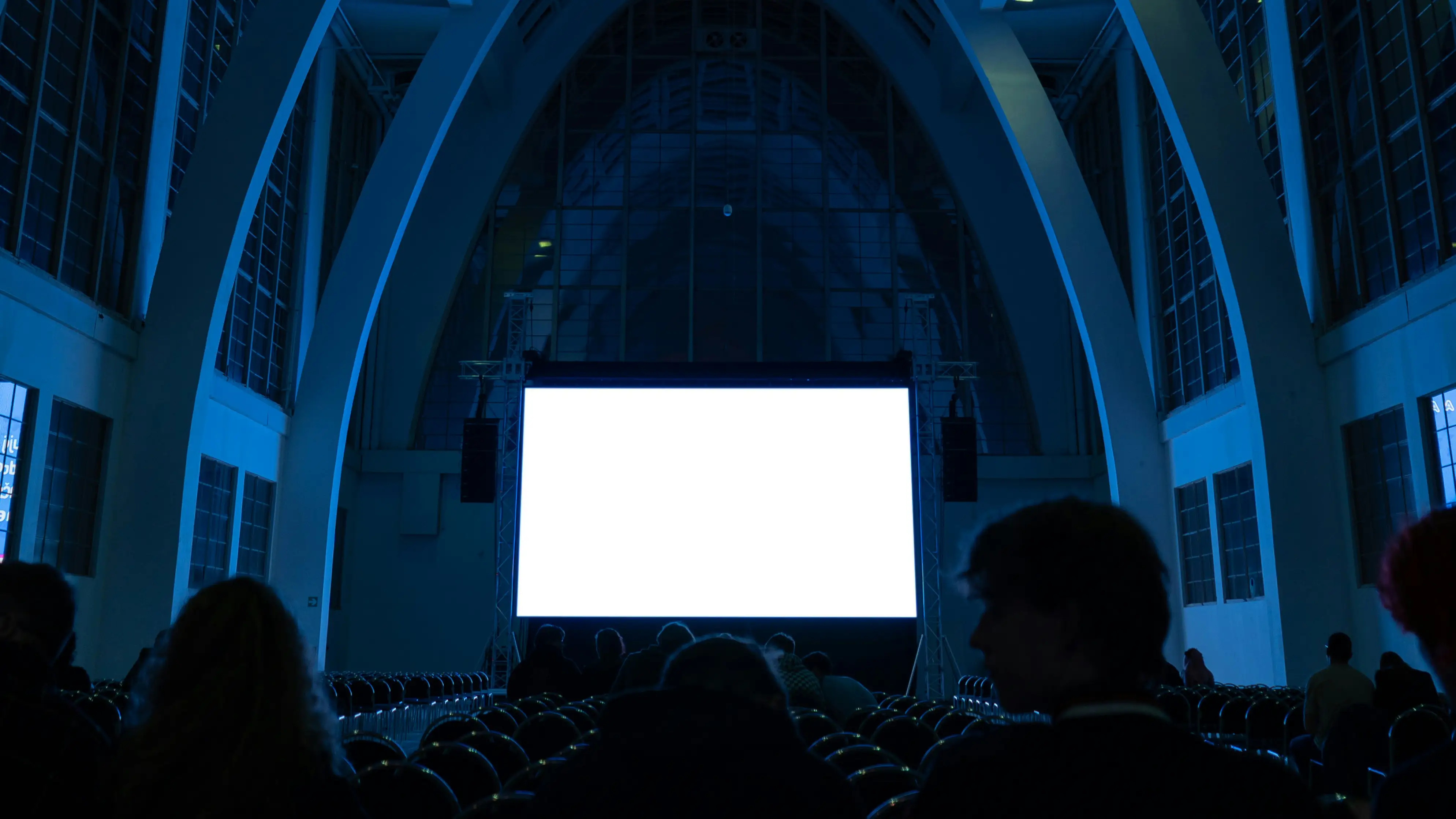 Audience silhouettes facing bright white screen in dark blue cinema hall
