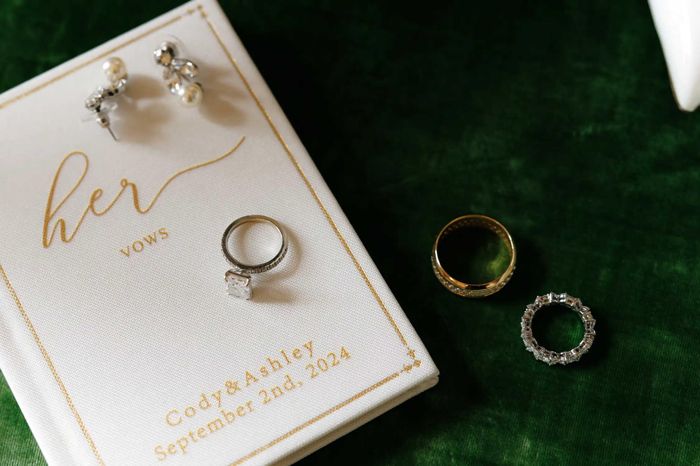 Wedding rings and vow book on green background with gold details