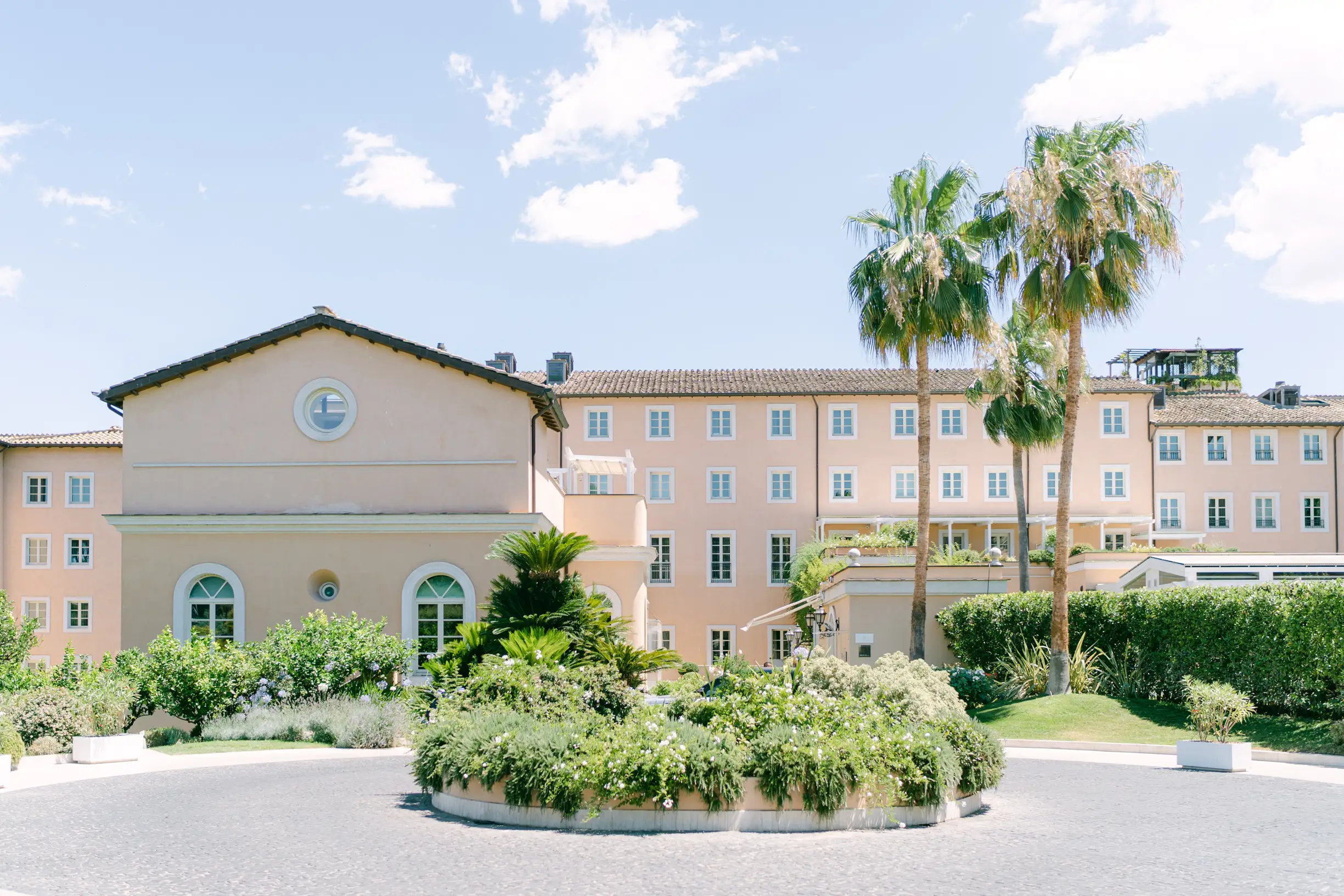 Elegant pastel hotel with palm trees and lush landscaped garden entrance