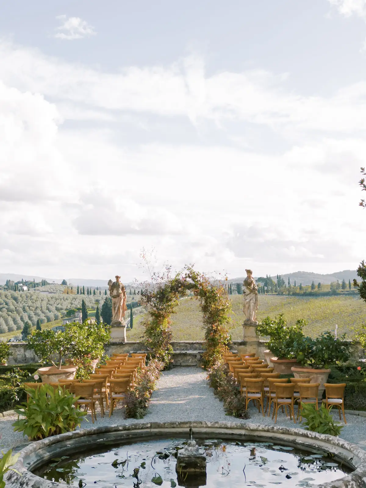 Outdoor wedding ceremony setup with floral arch overlooking Tuscan vineyard landscape
