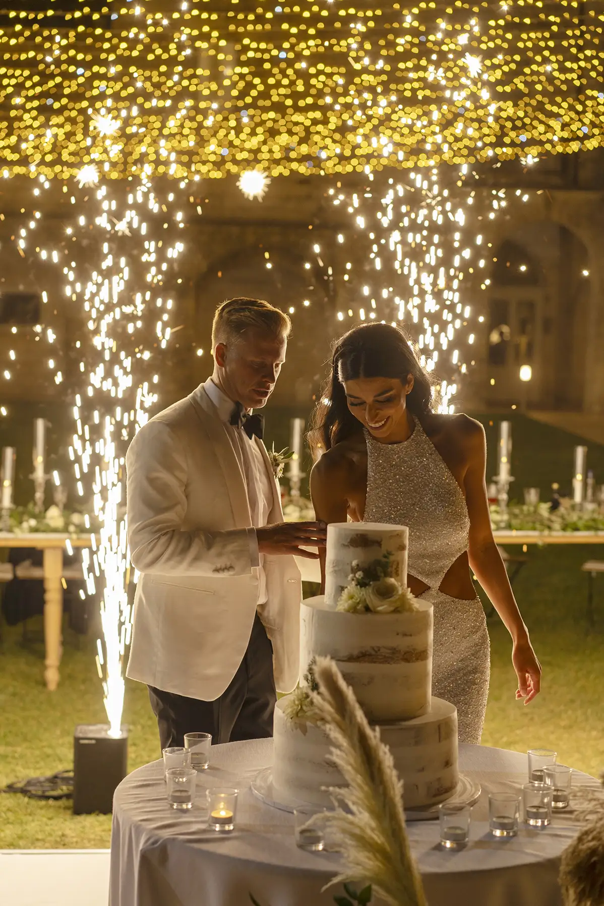 Wedding couple cutting cake under sparkling string lights at night