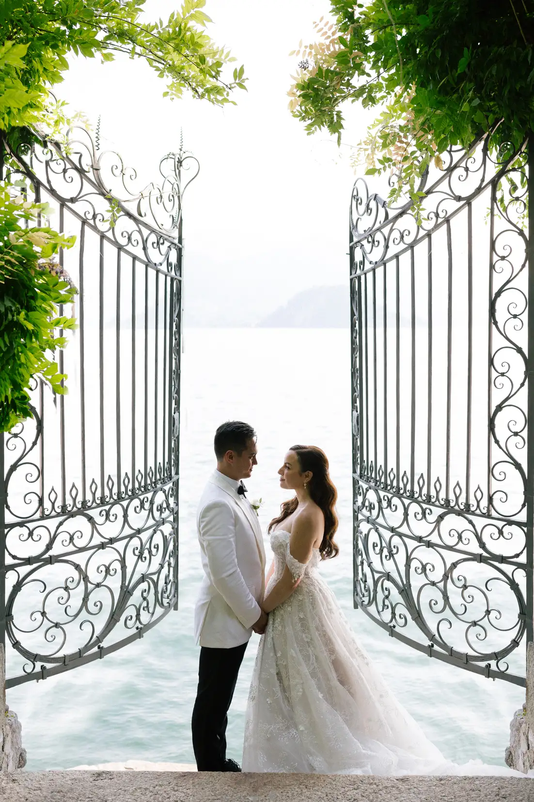 Wedding couple standing between ornate gates overlooking misty lake scenery