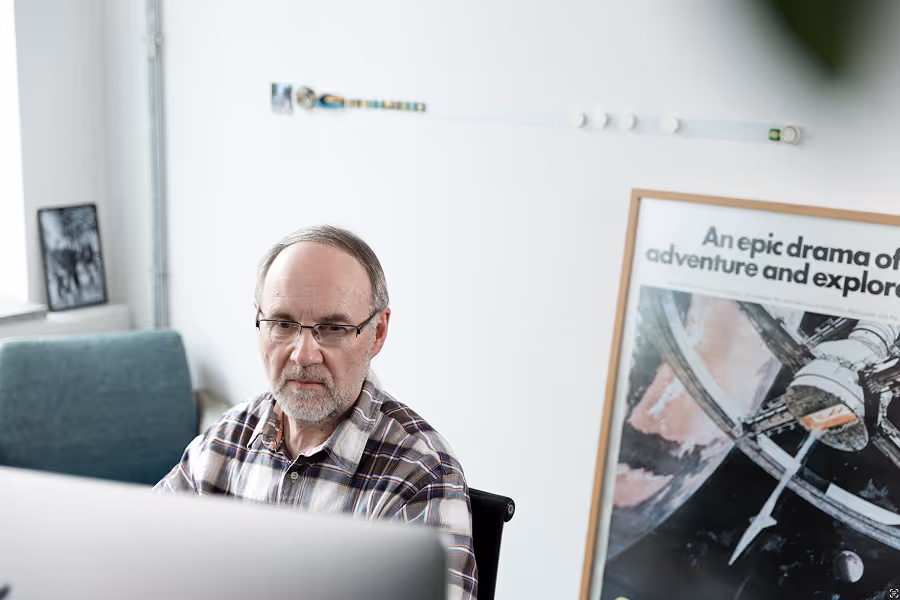 Middle-aged man with glasses working on a computer in a bright room with a space-themed poster.