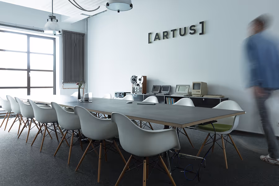 Modern conference room with long table, white chairs, retro electronics, and blurred person near wall.