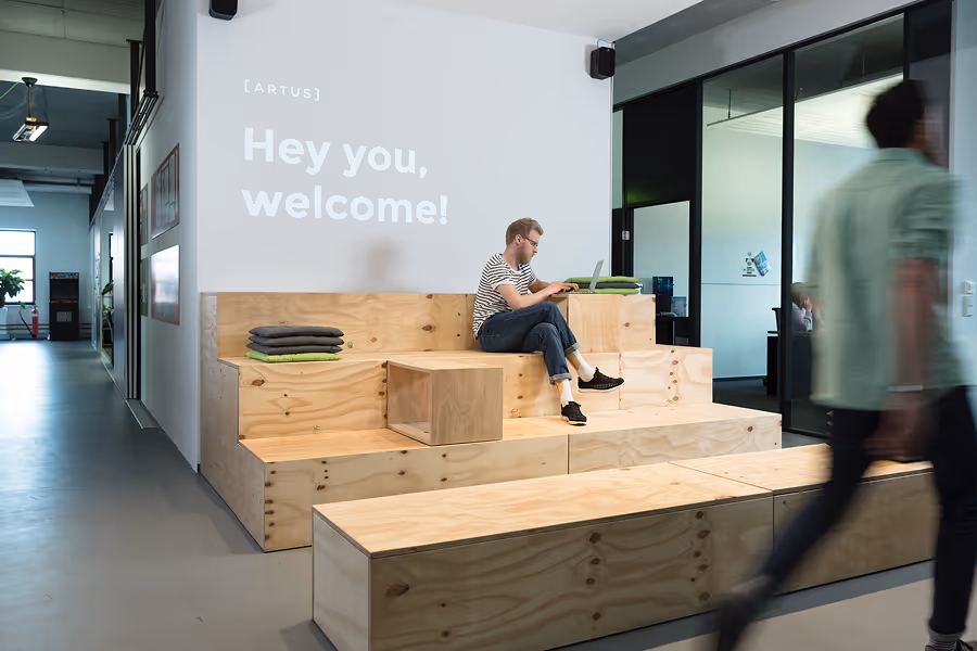 Man sitting on wooden stair seating in office lobby with projection reading 'Hey you, welcome!'