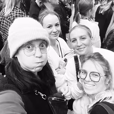 Four smiling Artus employees posing for a black and white selfie in a crowded indoor setting.