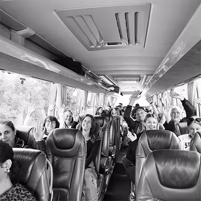 Group of Artus employees sitting in bus seats, smiling and waving at the camera.