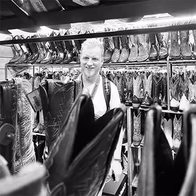 Artus employee smiling behind rows of cowboy boots in a store.