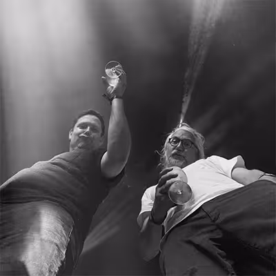 Low-angle photo of two Artus employees holding wine glasses and looking down at the camera.