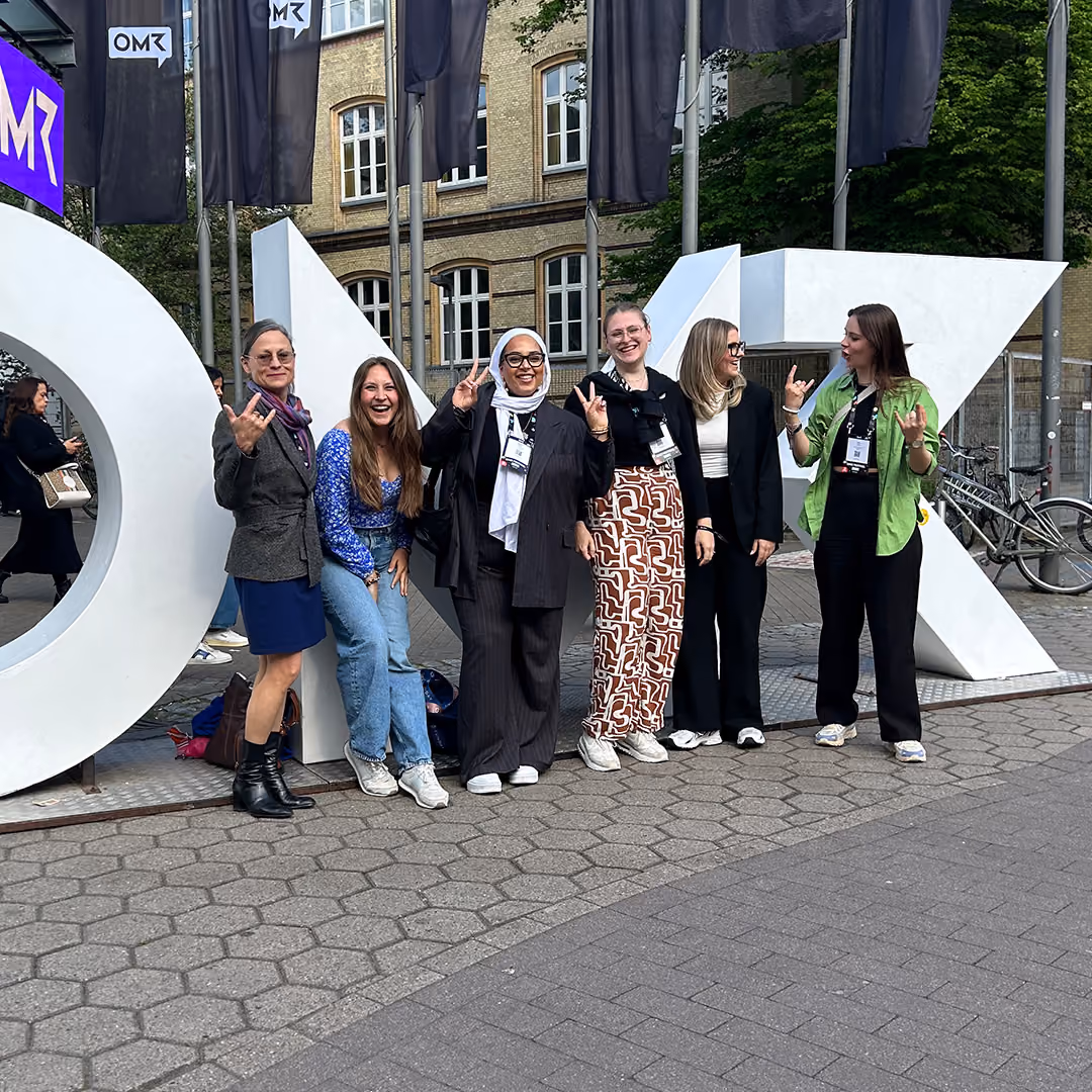 Group of six women smiling and posing in front of large white letters spelling OMR outdoors.