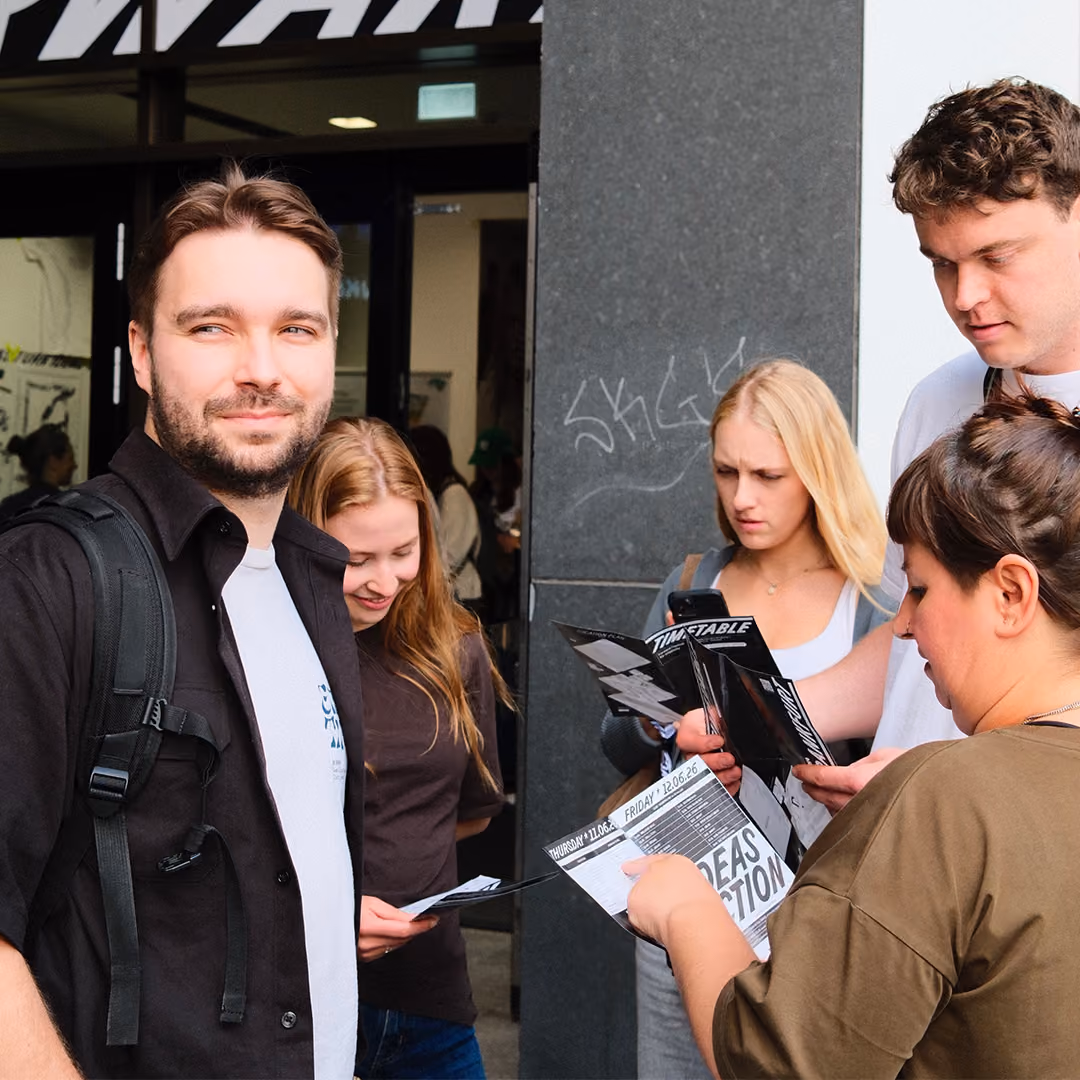 Group of five young people outside, some reading timetables and one smiling at the camera.