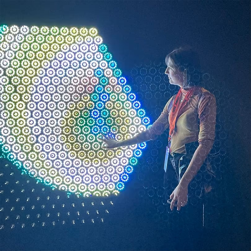 Woman touching a colorful hexagonal light installation glowing in a dark room.