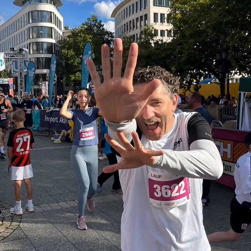 Smiling runner with race number 3622 reaching toward the camera during an outdoor event in a city.