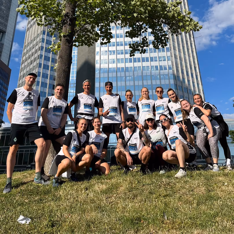 Group of runners in white shirts posing on grass with urban skyscrapers and blue sky behind.