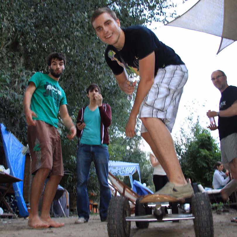 Young man on an off-road skateboard surrounded by friends outdoors in a casual setting.