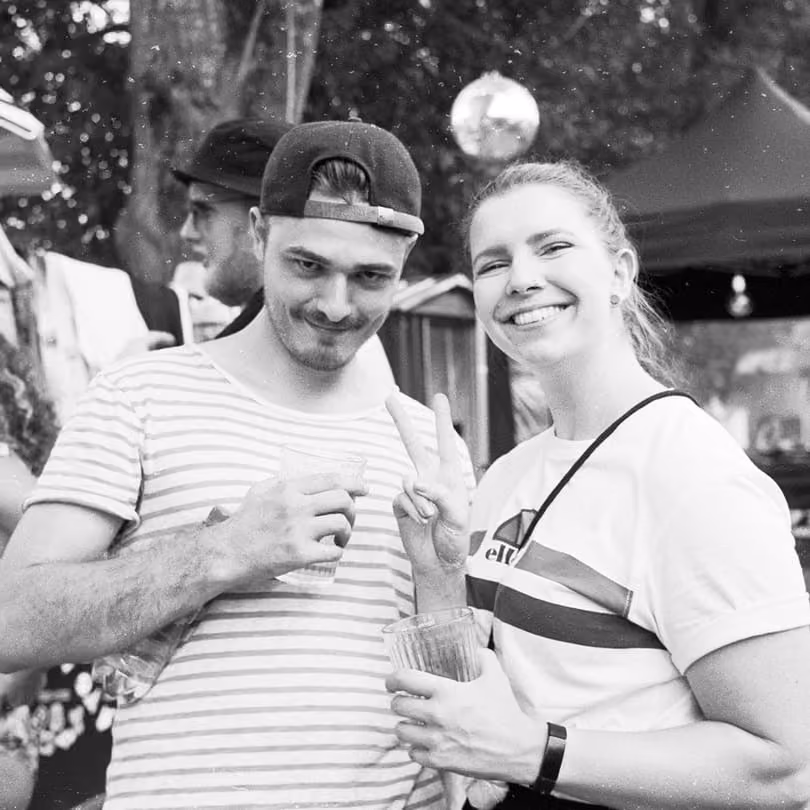 Black and white photo of a man and woman smiling and holding drinks at an outdoor event.