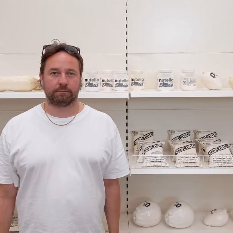 Man in white shirt stands in front of shelves displaying jars labeled Nutella and milk-style bags.