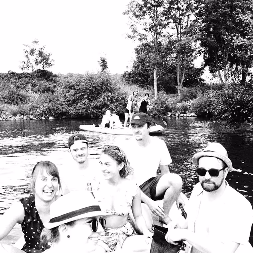 Group of people enjoying a sunny day on a paddle boat in a river with trees in the background.