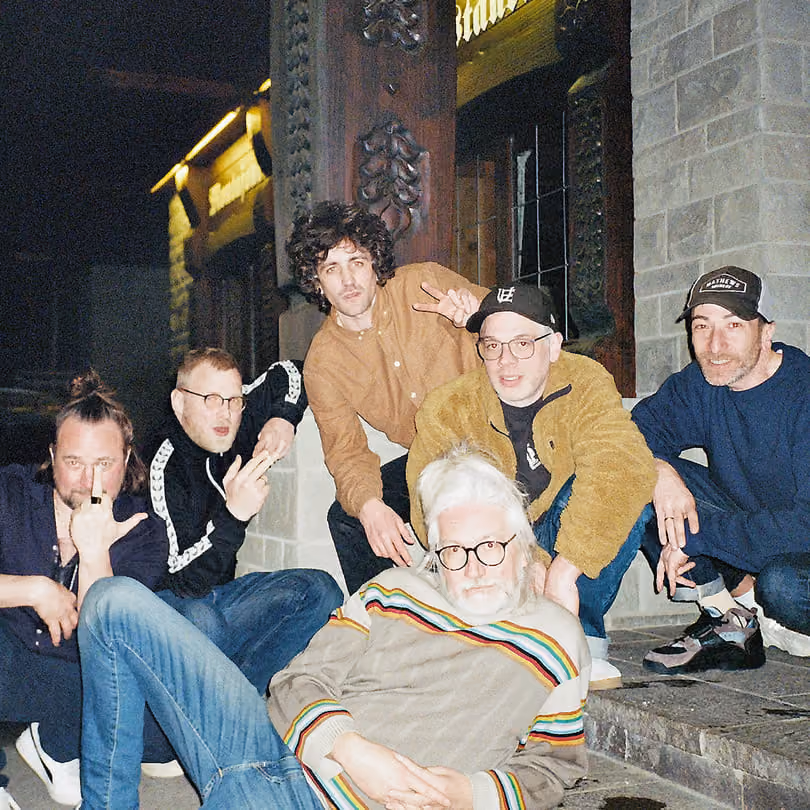 Six men posing casually outdoors at night near a stone building entrance.